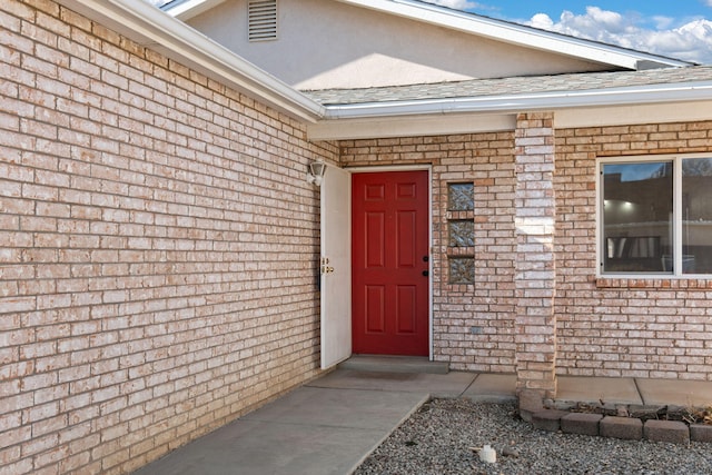 entrance to property featuring roof with shingles and brick siding