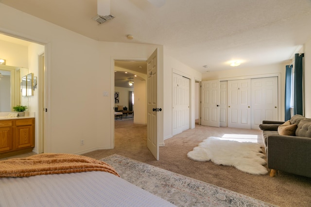 bedroom featuring visible vents, baseboards, light carpet, multiple closets, and ensuite bath