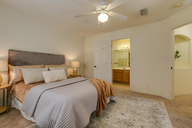 bedroom with ceiling fan, light colored carpet, visible vents, baseboards, and ensuite bath