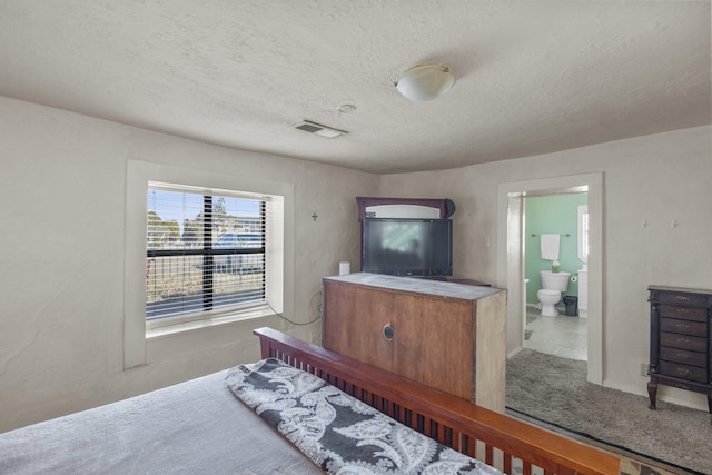 bedroom with ensuite bath, carpet, and a textured ceiling