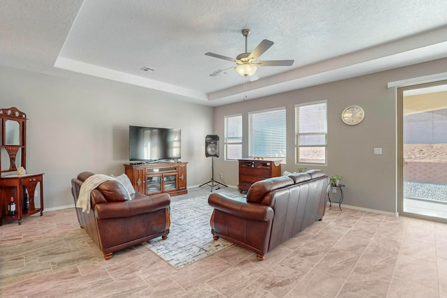 living room with a textured ceiling, a tray ceiling, and ceiling fan