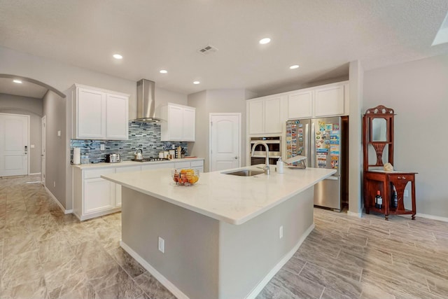 kitchen with wall chimney exhaust hood, sink, a kitchen island with sink, and appliances with stainless steel finishes