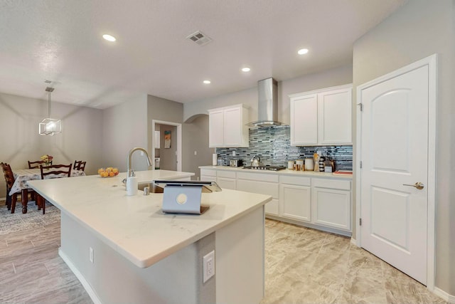 kitchen with white cabinets, pendant lighting, a center island with sink, and wall chimney exhaust hood