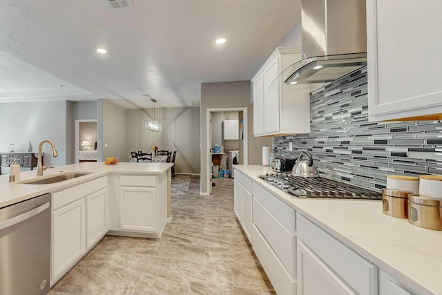 kitchen featuring white cabinets, wall chimney range hood, sink, decorative light fixtures, and stainless steel appliances