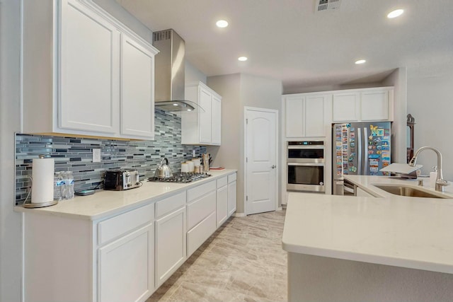 kitchen featuring white cabinets, wall chimney range hood, sink, and appliances with stainless steel finishes