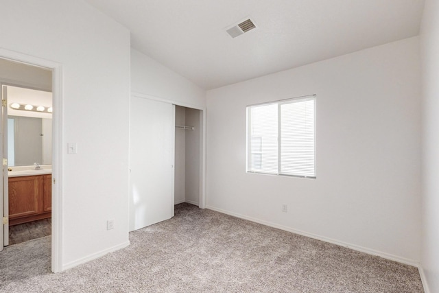 unfurnished bedroom featuring connected bathroom, a closet, light colored carpet, and lofted ceiling