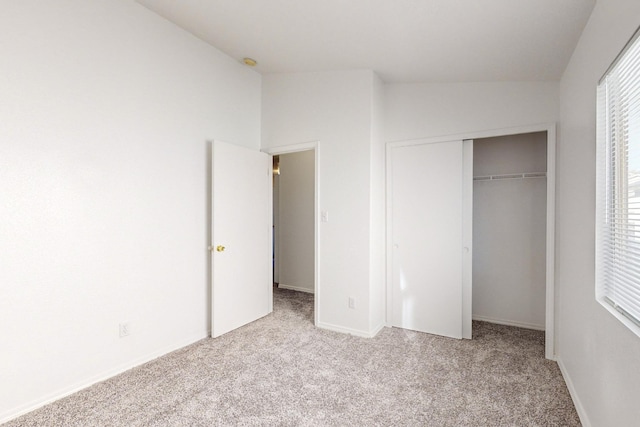 unfurnished bedroom featuring light colored carpet, a closet, and lofted ceiling