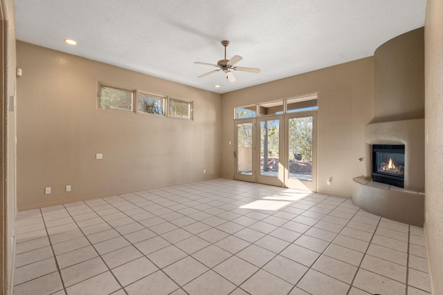 unfurnished living room featuring ceiling fan, a fireplace, light tile patterned floors, and a textured ceiling