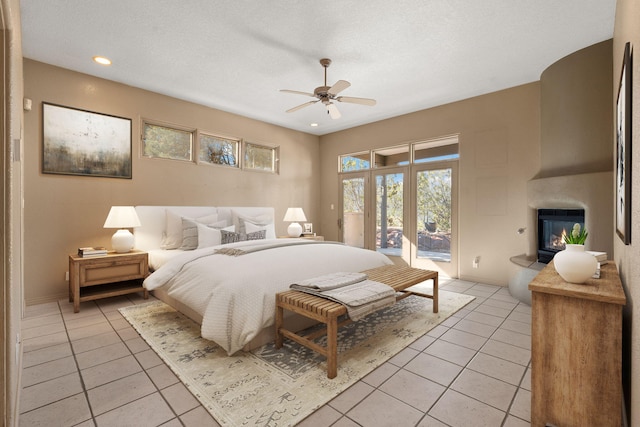 tiled bedroom featuring ceiling fan, a large fireplace, a textured ceiling, and access to outside