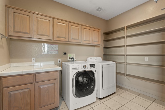 laundry room featuring washing machine and dryer, light tile patterned floors, and cabinets