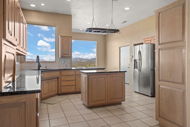 kitchen featuring sink, light tile patterned floors, stainless steel fridge with ice dispenser, a textured ceiling, and a kitchen island