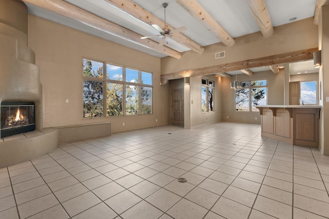 unfurnished living room featuring beamed ceiling, a large fireplace, ceiling fan, and light tile patterned flooring