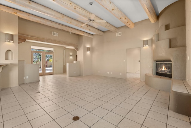 unfurnished living room with ceiling fan, french doors, light tile patterned flooring, and beamed ceiling