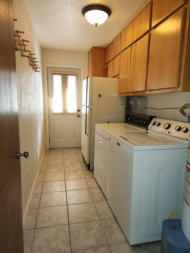 clothes washing area with cabinets, light tile patterned floors, a textured ceiling, and washer and clothes dryer