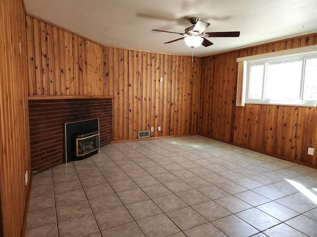 unfurnished living room with light tile patterned floors, a wood stove, ceiling fan, and wooden walls