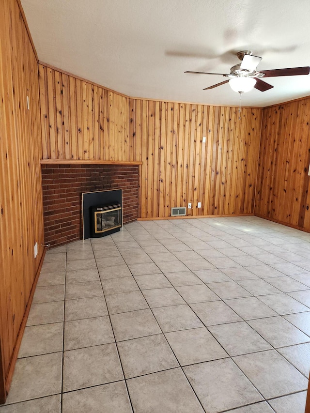 unfurnished living room featuring light tile patterned floors, a wood stove, ceiling fan, and wooden walls