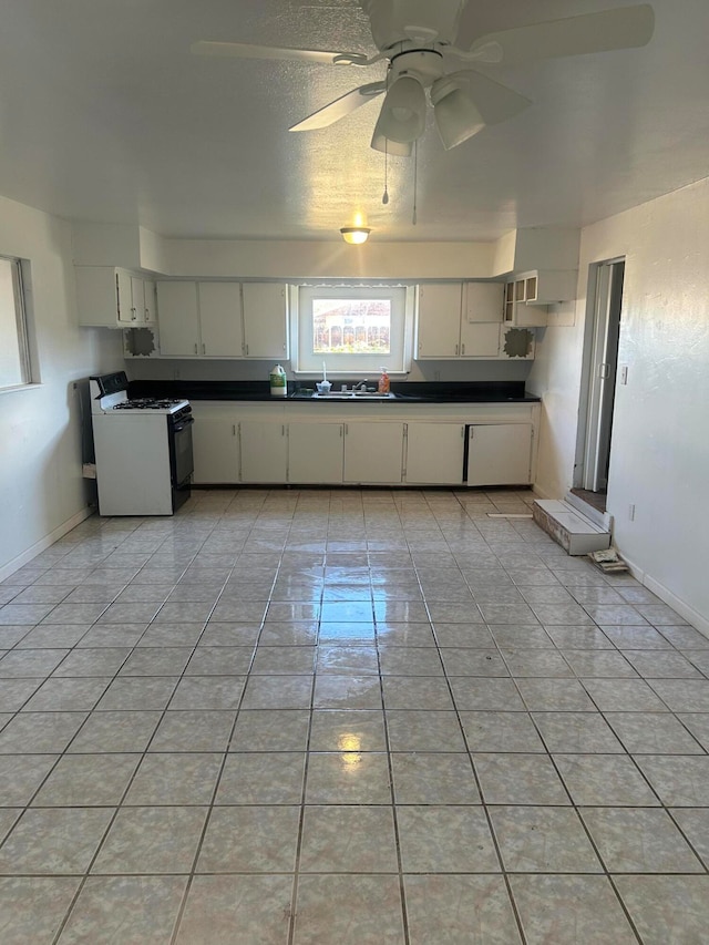 kitchen featuring white cabinets, sink, ceiling fan, white gas range, and light tile patterned flooring