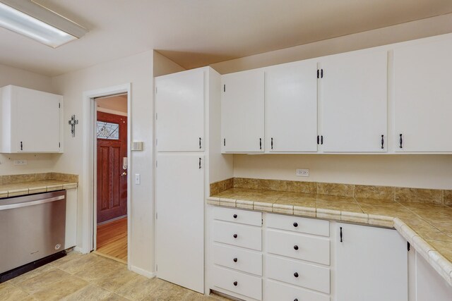 kitchen with tile counters, stainless steel dishwasher, and white cabinets