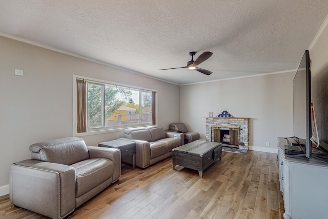 living room featuring a textured ceiling, ornamental molding, ceiling fan, a fireplace, and light hardwood / wood-style floors