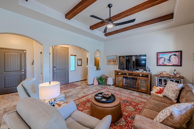 living area with arched walkways, ceiling fan, a high ceiling, a tray ceiling, and beam ceiling