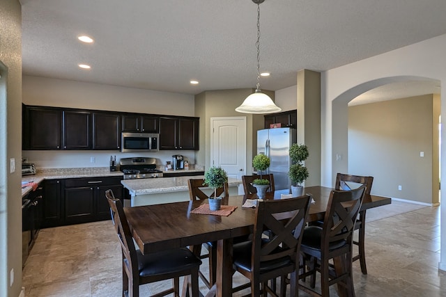 kitchen featuring pendant lighting, a textured ceiling, appliances with stainless steel finishes, dark brown cabinets, and a kitchen island