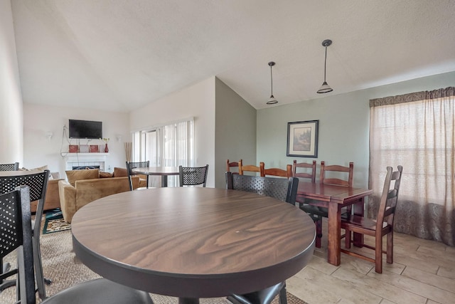 dining room featuring a tiled fireplace, lofted ceiling, and a textured ceiling