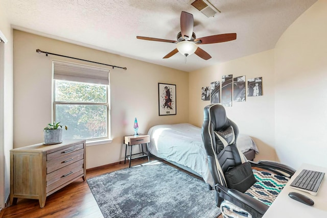 bedroom with a textured ceiling, ceiling fan, and dark wood-type flooring