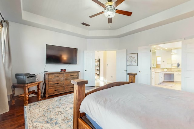 bedroom with a tray ceiling, ensuite bath, ceiling fan, and light hardwood / wood-style floors