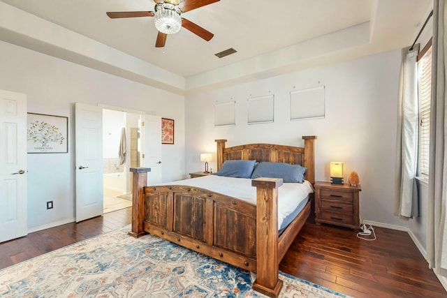 bedroom featuring dark hardwood / wood-style floors, ceiling fan, a raised ceiling, and connected bathroom