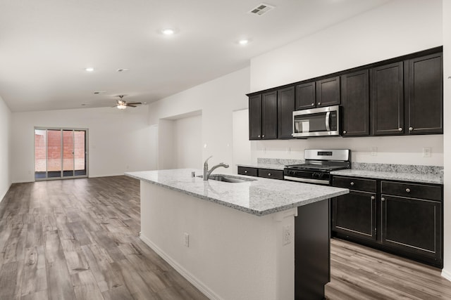 kitchen with sink, stainless steel appliances, light hardwood / wood-style flooring, vaulted ceiling, and a center island with sink