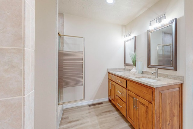 bathroom featuring a textured ceiling, vanity, wood-type flooring, and a shower with door