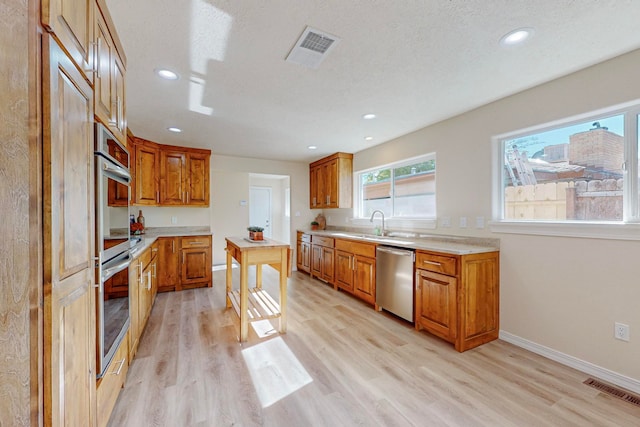 kitchen with a textured ceiling, light wood-type flooring, stainless steel appliances, and sink