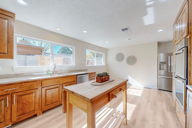 kitchen with a textured ceiling, light wood-type flooring, stainless steel appliances, and sink