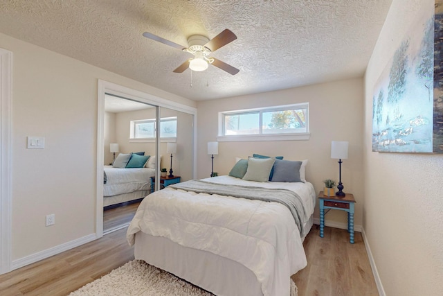 bedroom with a textured ceiling, light hardwood / wood-style floors, a closet, and ceiling fan