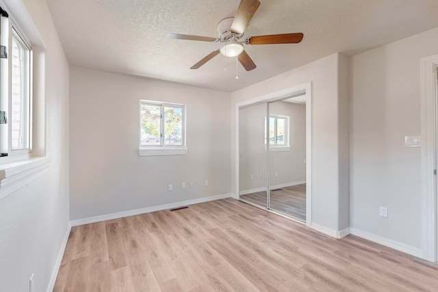 unfurnished bedroom with ceiling fan, light hardwood / wood-style floors, a textured ceiling, and a closet