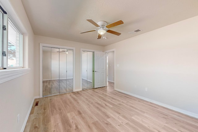 unfurnished bedroom featuring ceiling fan, light wood-type flooring, and multiple closets