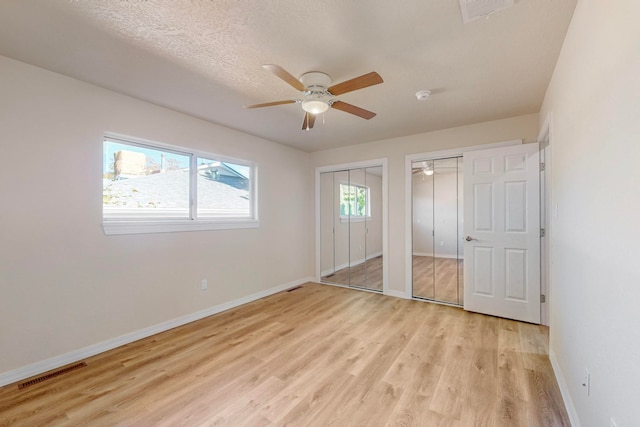 unfurnished bedroom with a textured ceiling, ceiling fan, two closets, and light wood-type flooring