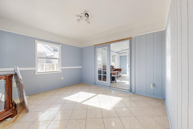 empty room featuring wood walls, french doors, and light tile patterned flooring