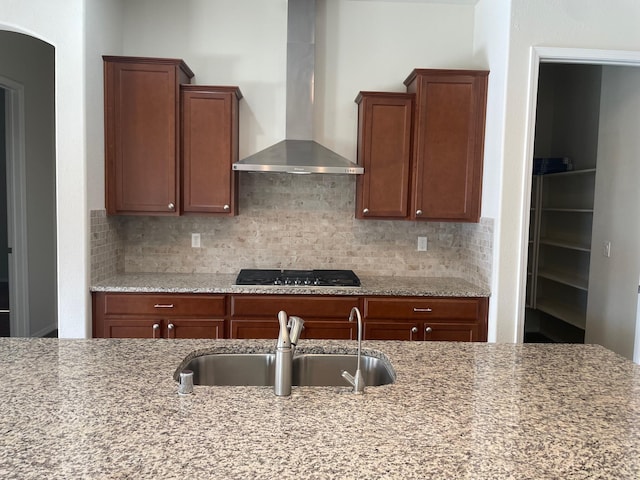 kitchen featuring light stone counters, black gas stovetop, wall chimney exhaust hood, and sink