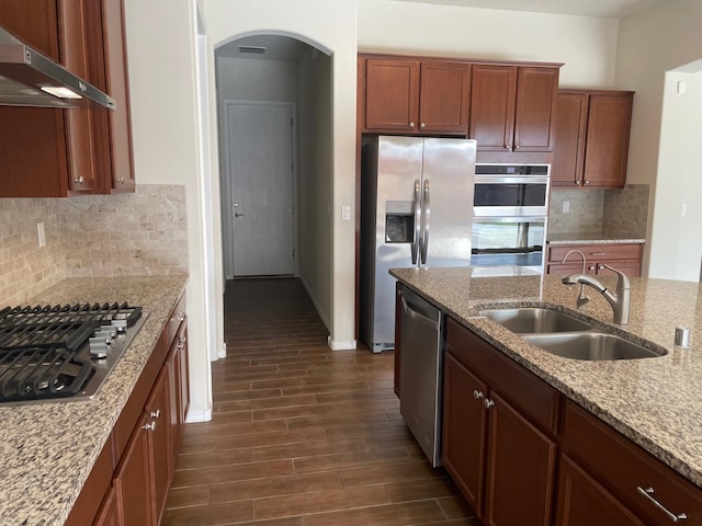 kitchen with appliances with stainless steel finishes, dark hardwood / wood-style flooring, light stone counters, exhaust hood, and sink