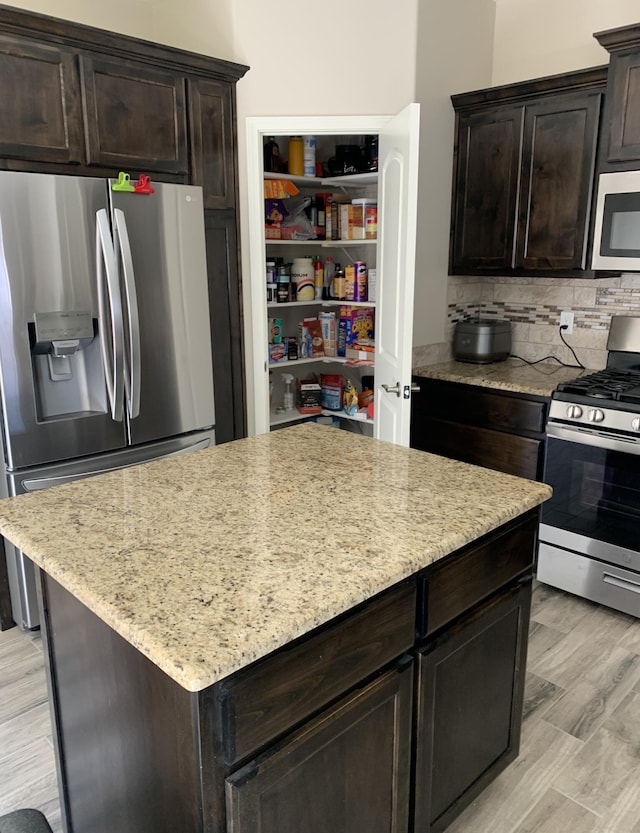 kitchen featuring light stone countertops, stainless steel appliances, light hardwood / wood-style flooring, backsplash, and dark brown cabinets