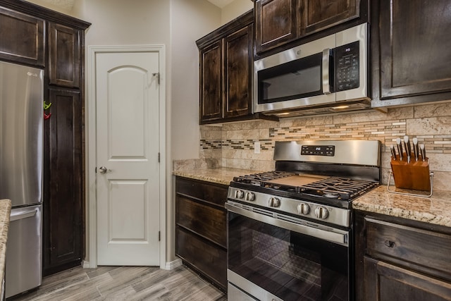 kitchen with dark brown cabinetry, light stone countertops, tasteful backsplash, appliances with stainless steel finishes, and light wood-type flooring