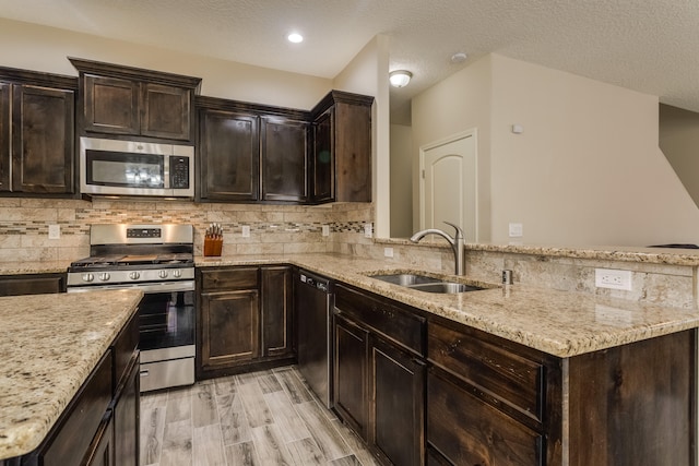 kitchen with sink, a textured ceiling, appliances with stainless steel finishes, tasteful backsplash, and light hardwood / wood-style floors