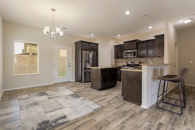 kitchen featuring appliances with stainless steel finishes, a textured ceiling, decorative light fixtures, a chandelier, and light hardwood / wood-style floors