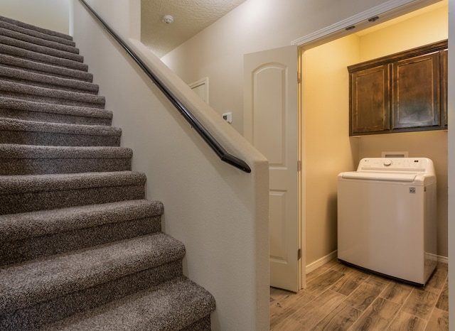 laundry room featuring cabinets, washer / dryer, light wood-type flooring, and a textured ceiling