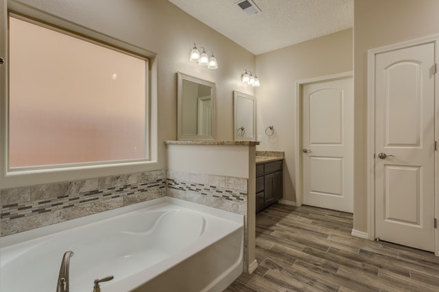 bathroom featuring vanity, wood-type flooring, a textured ceiling, and a bathtub