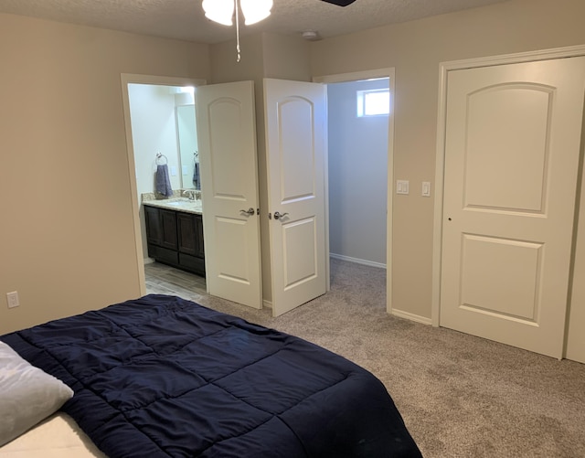 carpeted bedroom with ensuite bathroom, ceiling fan, sink, and a textured ceiling