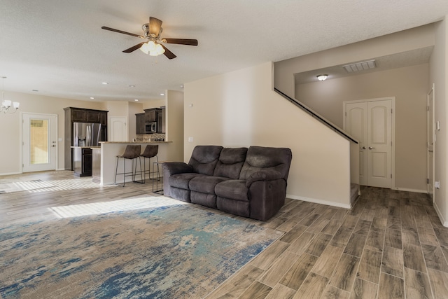 living room with hardwood / wood-style flooring, ceiling fan with notable chandelier, and a textured ceiling