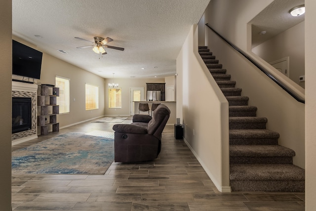 living room featuring a textured ceiling, a tiled fireplace, ceiling fan with notable chandelier, and hardwood / wood-style flooring