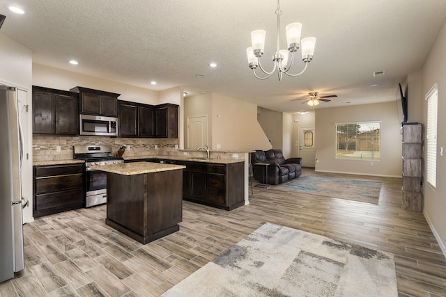 kitchen with sink, a center island, hanging light fixtures, stainless steel appliances, and light hardwood / wood-style floors